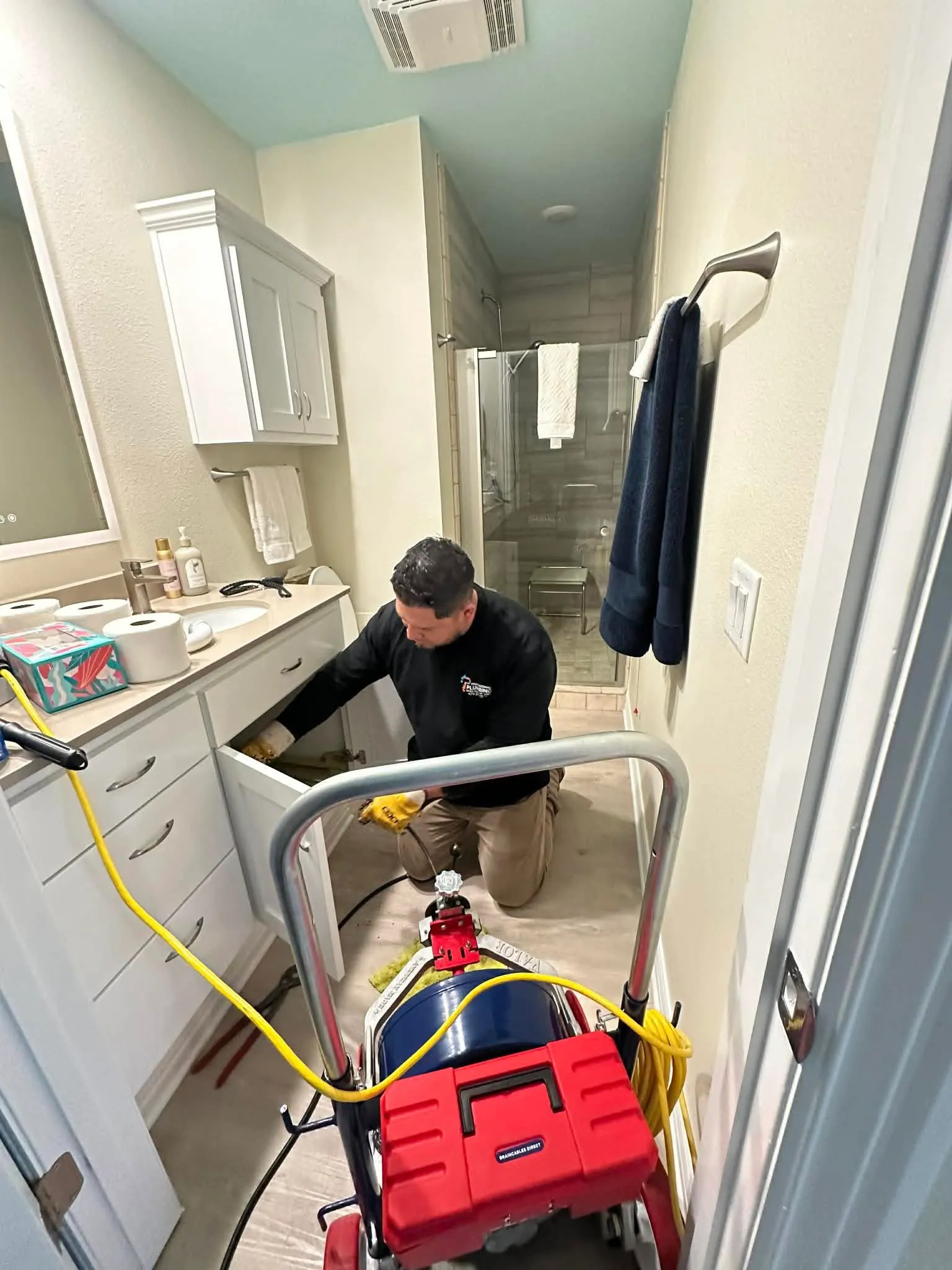 Plumber performing drain cleaning service under a bathroom vanity